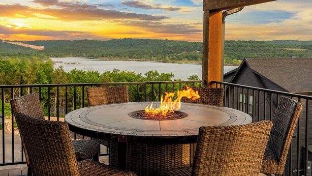 A round table with a fire pit, surrounded by wicker chairs, on a balcony with a view of a lake and hills. - Your Relaxation Destination at Emerald Shores (Hollister)