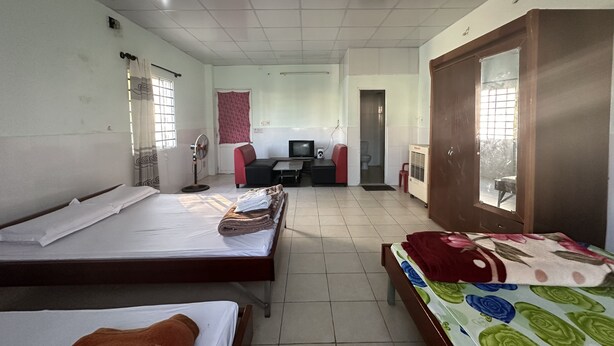 Um quarto com duas camas, uma escrivaninha com computador, uma cadeira, uma janela e uma porta.