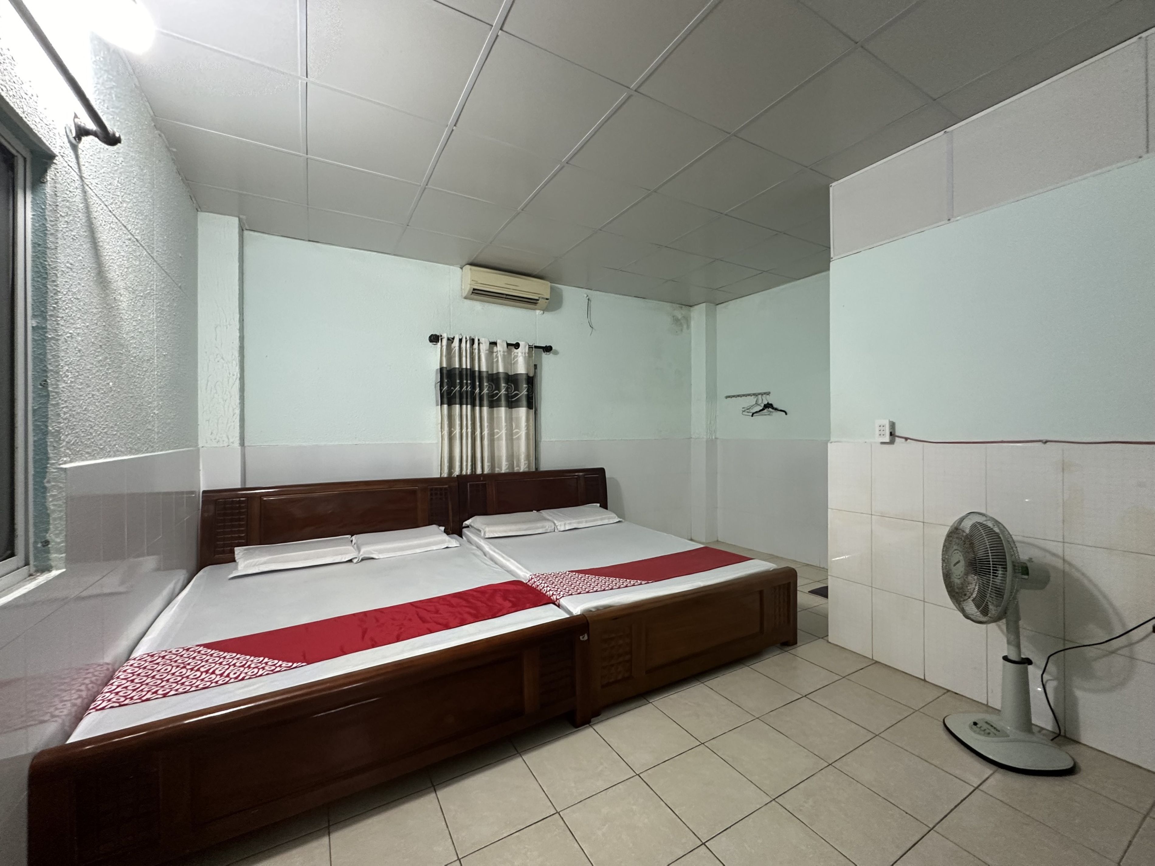 Una habitación con una cama grande, un ventilador de pie y una ventana con cortinas.