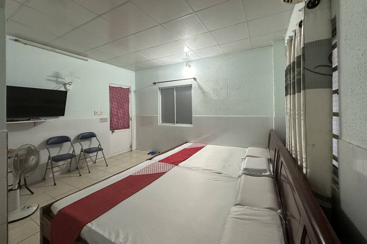 A hotel room with a bed, a TV, a window, and a fan.