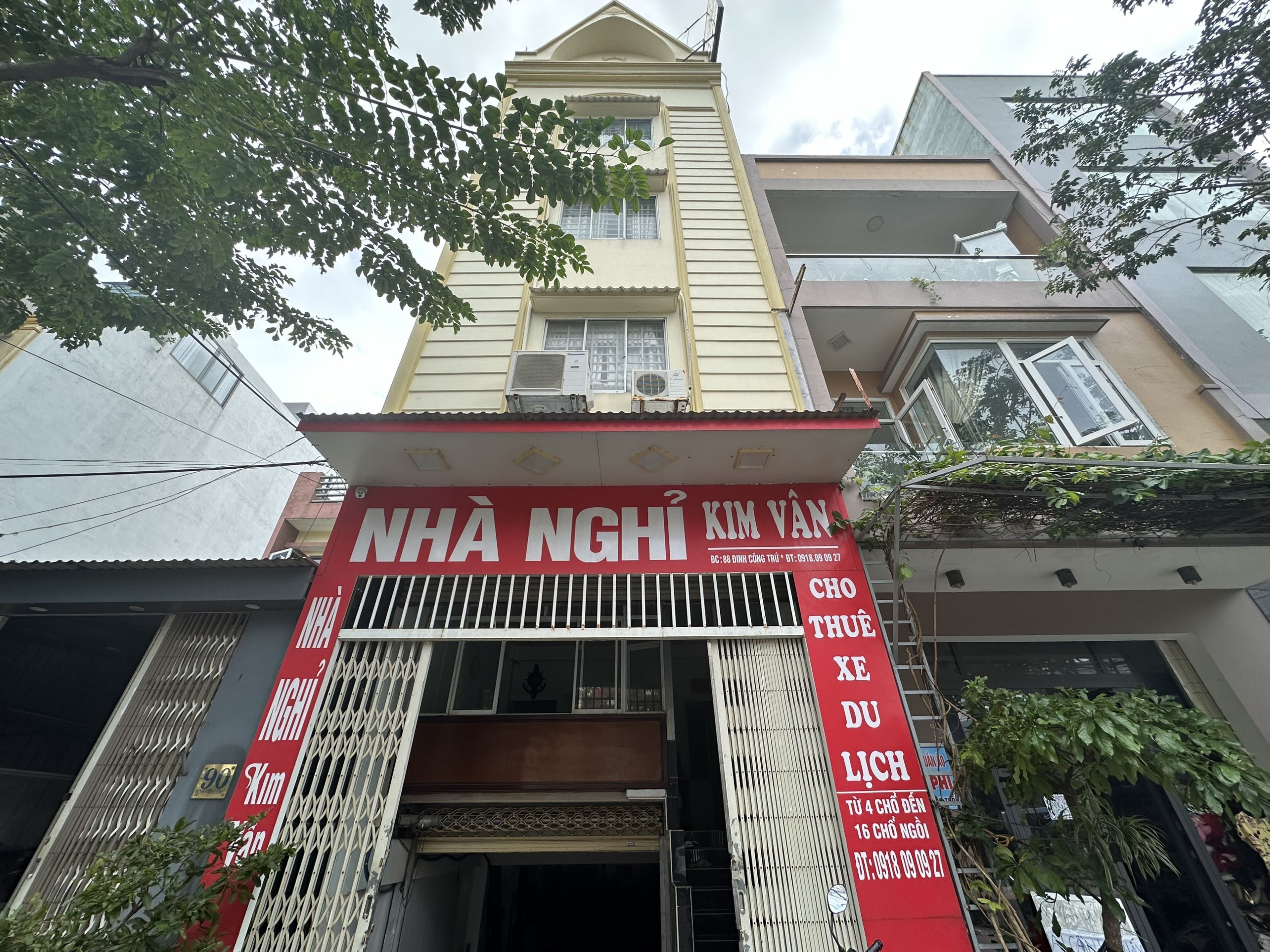 Un edificio con un letrero rojo y blanco, una entrada con reja y una escalera que lleva a los pisos superiores.