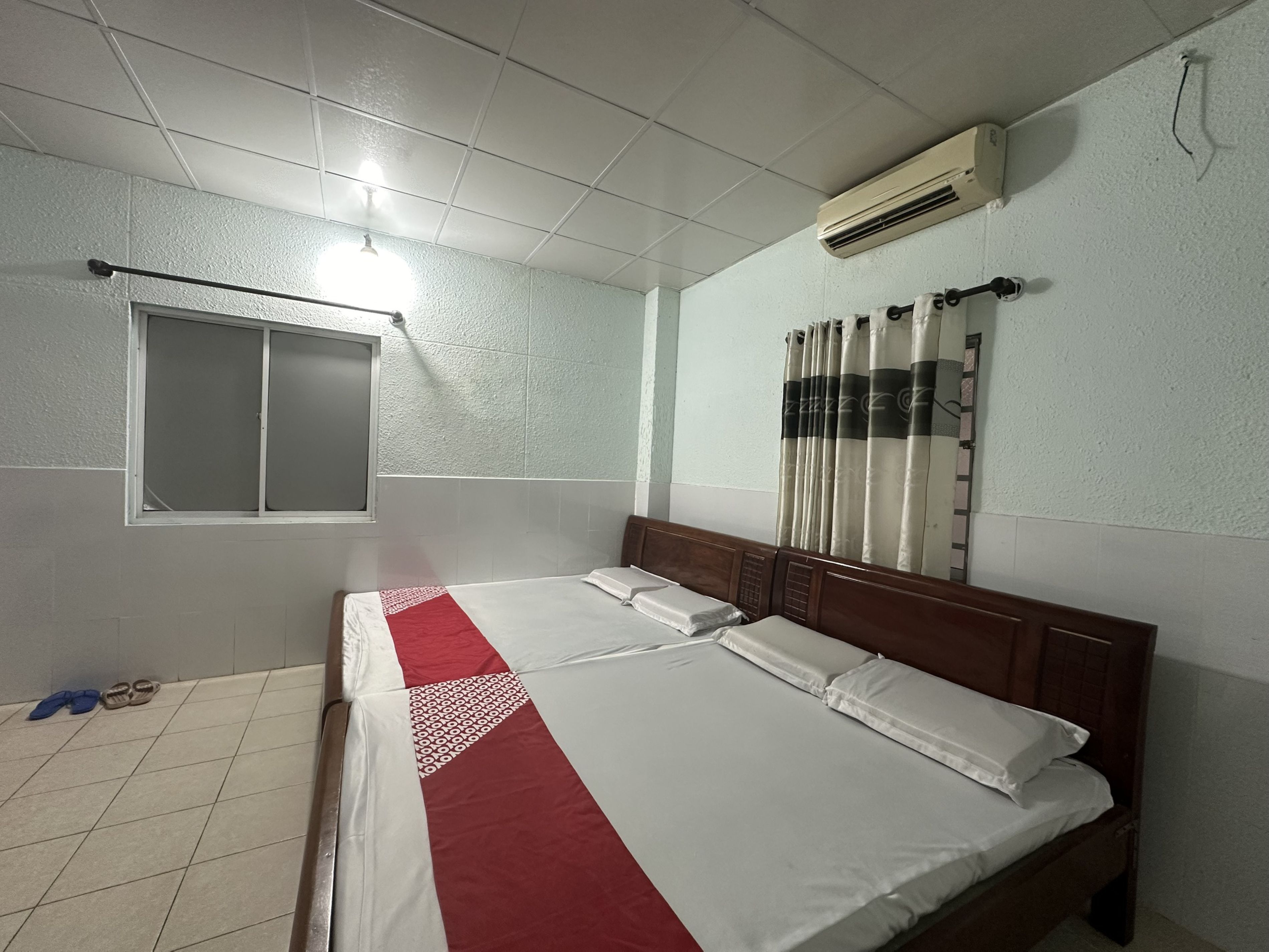 A bedroom with a bed, a window, an air conditioner, and a curtain.