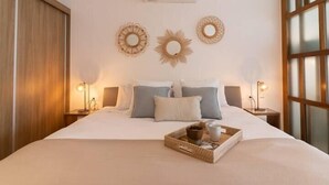 A neatly made bed with a tray of breakfast items, two wall-mounted decorative mirrors, and a window with blinds. - Apartments near the beach pool and gym (Playa del Carmen)