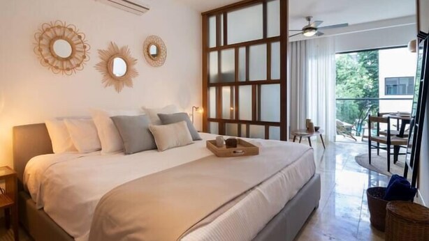 A spacious bedroom with a large bed, a balcony with a table and chairs, and decorative wall mirrors. - Apartments near the beach pool and gym (Playa del Carmen)