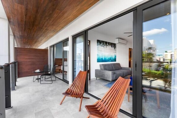 A modern interior with a wooden ceiling, a glass door leading to a balcony, and a grey sofa.