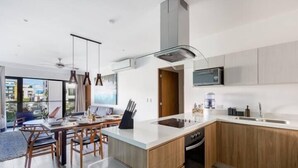 A modern kitchen with wooden cabinets, a built-in microwave, and a dining area with a table and chairs. - Apartments near the beach pool and gym (Playa del Carmen)