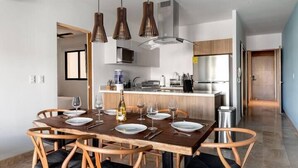 A modern dining area with a wooden table set for six, surrounded by wicker chairs. - Apartments near the beach pool and gym (Playa del Carmen)