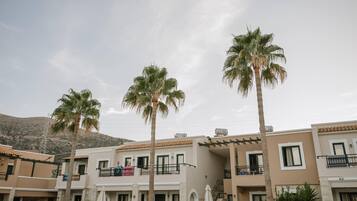 A residential building with multiple balconies, palm trees, and a mountainous backdrop.
