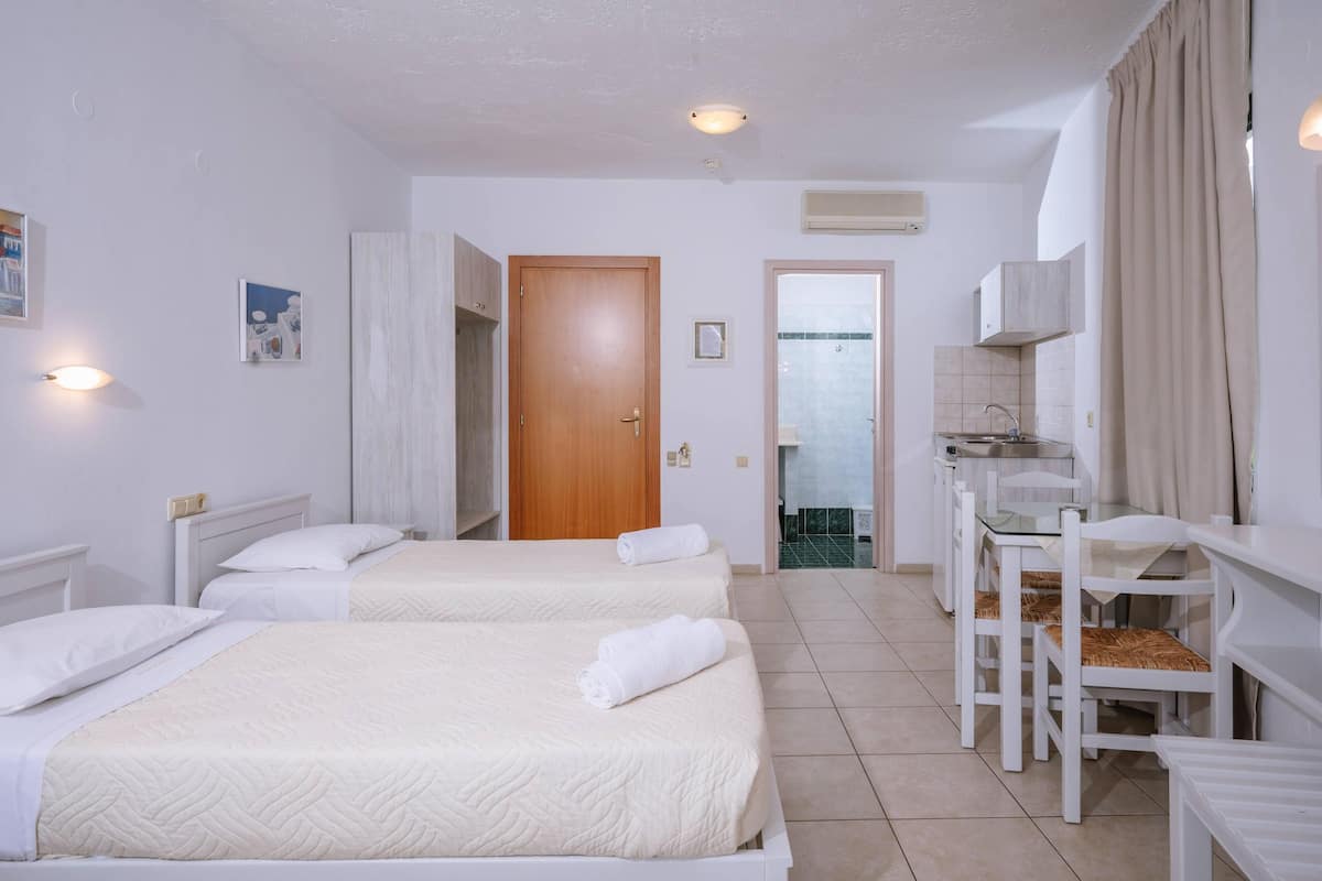 Habitación de hotel con dos camas, baño, una pequeña cocina y una zona de estar con mesa y sillas.