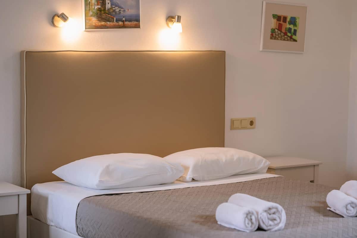 Una cama bien hecha con sábanas y almohadas blancas, una mesita de noche y dos lámparas de pared.