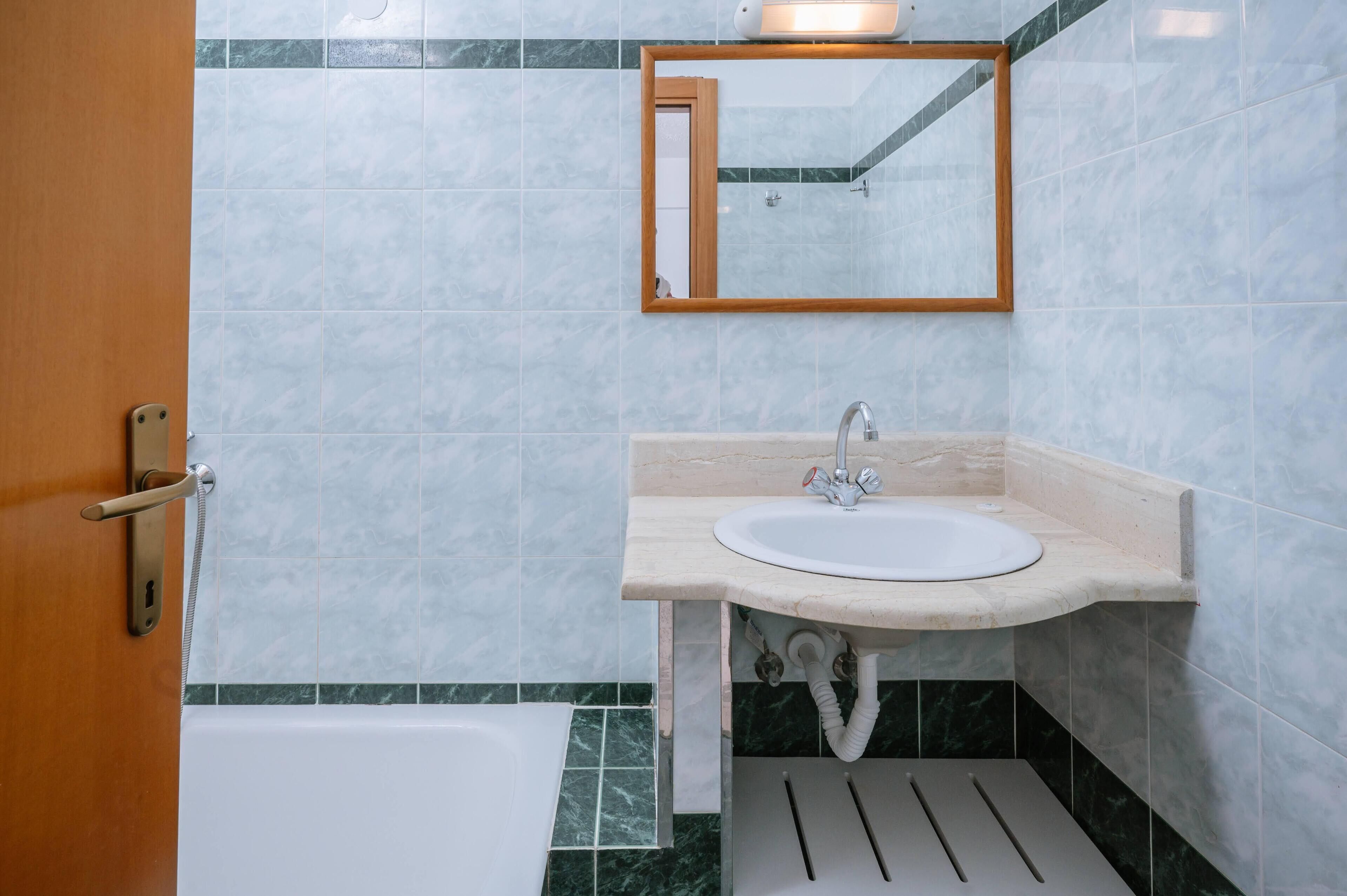 A bathroom with a sink, mirror, and bathtub.