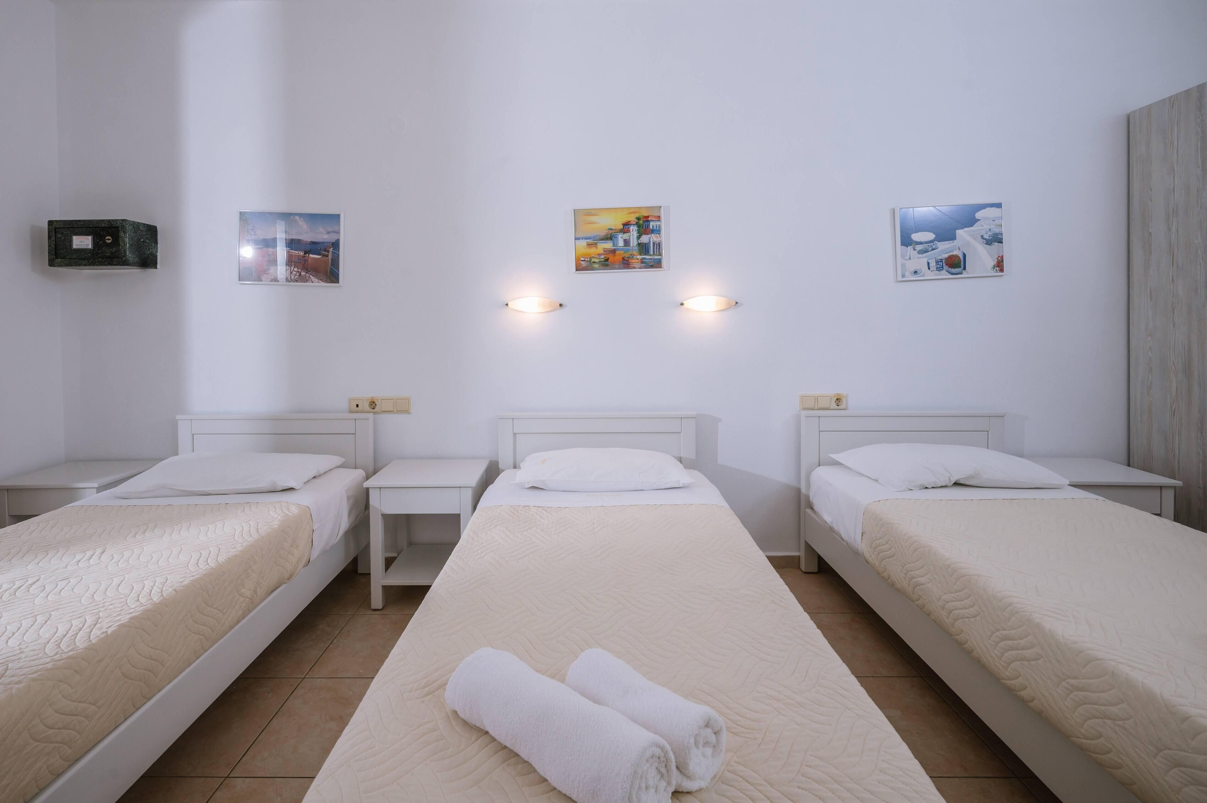 A hotel room with three single beds, a large bed, and a small table between the beds.