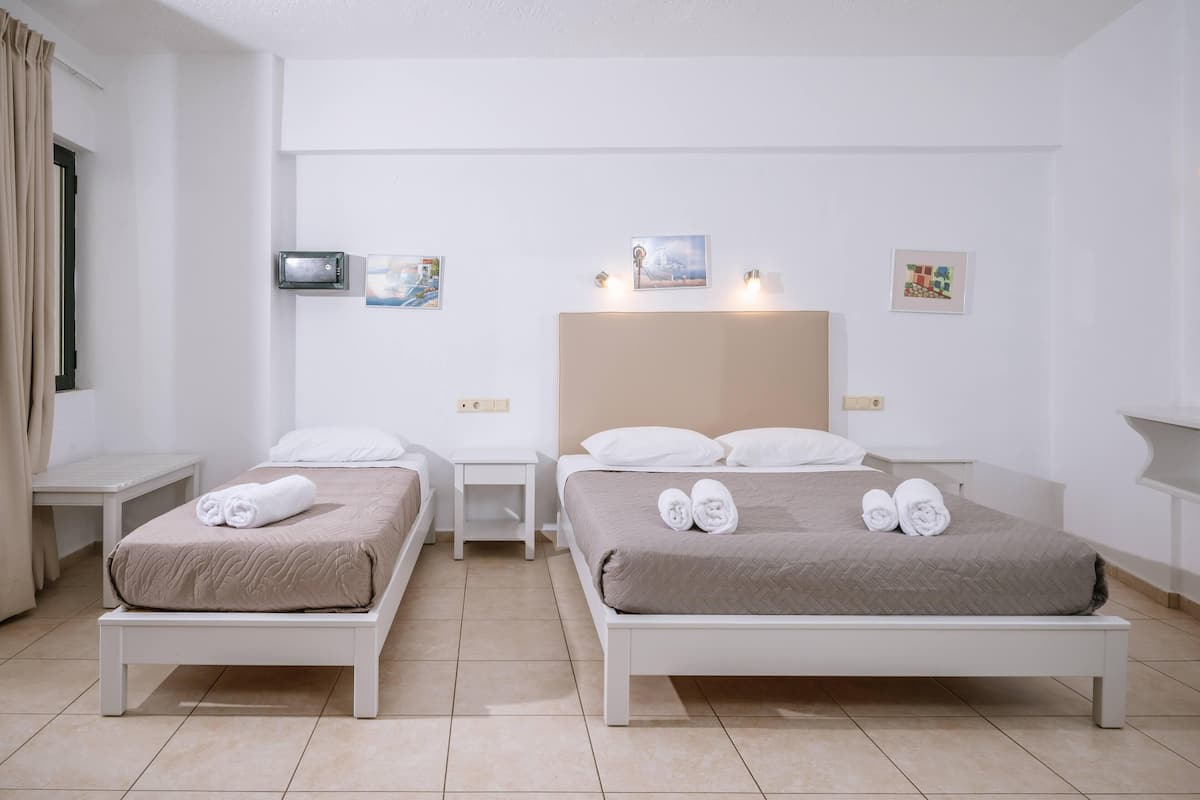 Habitación de hotel con dos camas individuales, una cama grande, televisión y obras de arte en las paredes.