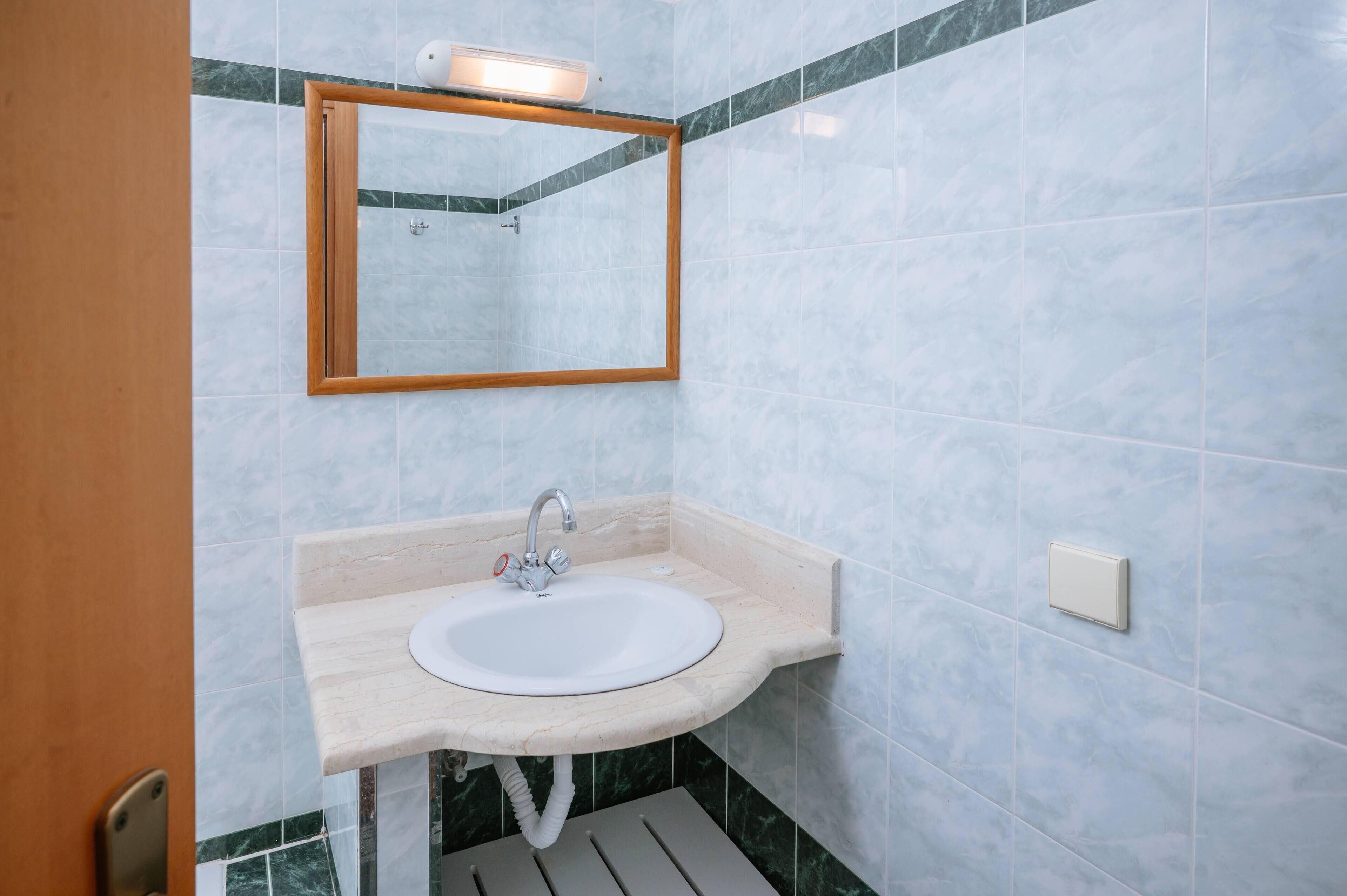 A bathroom with a marble sink, a wooden-framed mirror, and a light fixture above the mirror.
