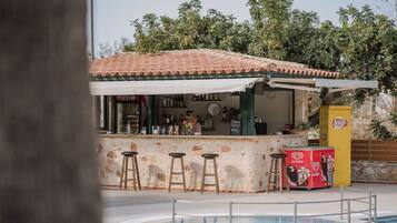 A poolside bar with stools, a Coca-Cola refrigerator, and a Lay's snack machine.