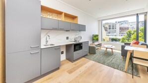 A modern kitchen with grey cabinets, a white countertop, and a built-in microwave. There is a window with a view of buildings and greenery. - Comfortable Studio With City Views (Cape Town)