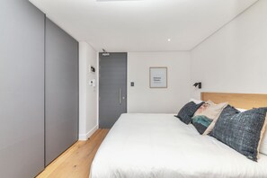A modern bedroom with a large bed, grey wardrobe, and a framed artwork on the wall.