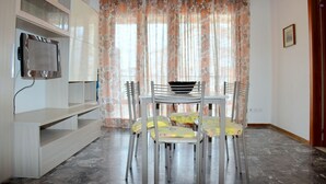 A dining area with a table and chairs, a television mounted on the wall, and a patterned curtain. - For Your Getaway Near the Beach-beahost Rentals (San Michele al Tagliamento)