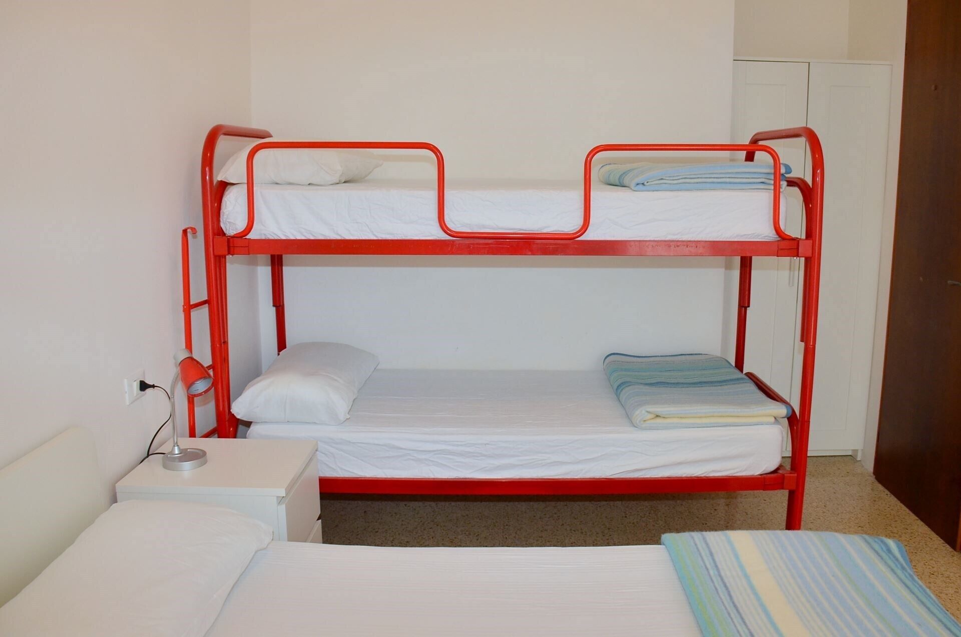 A bunk bed with white bedding and a red metal frame.