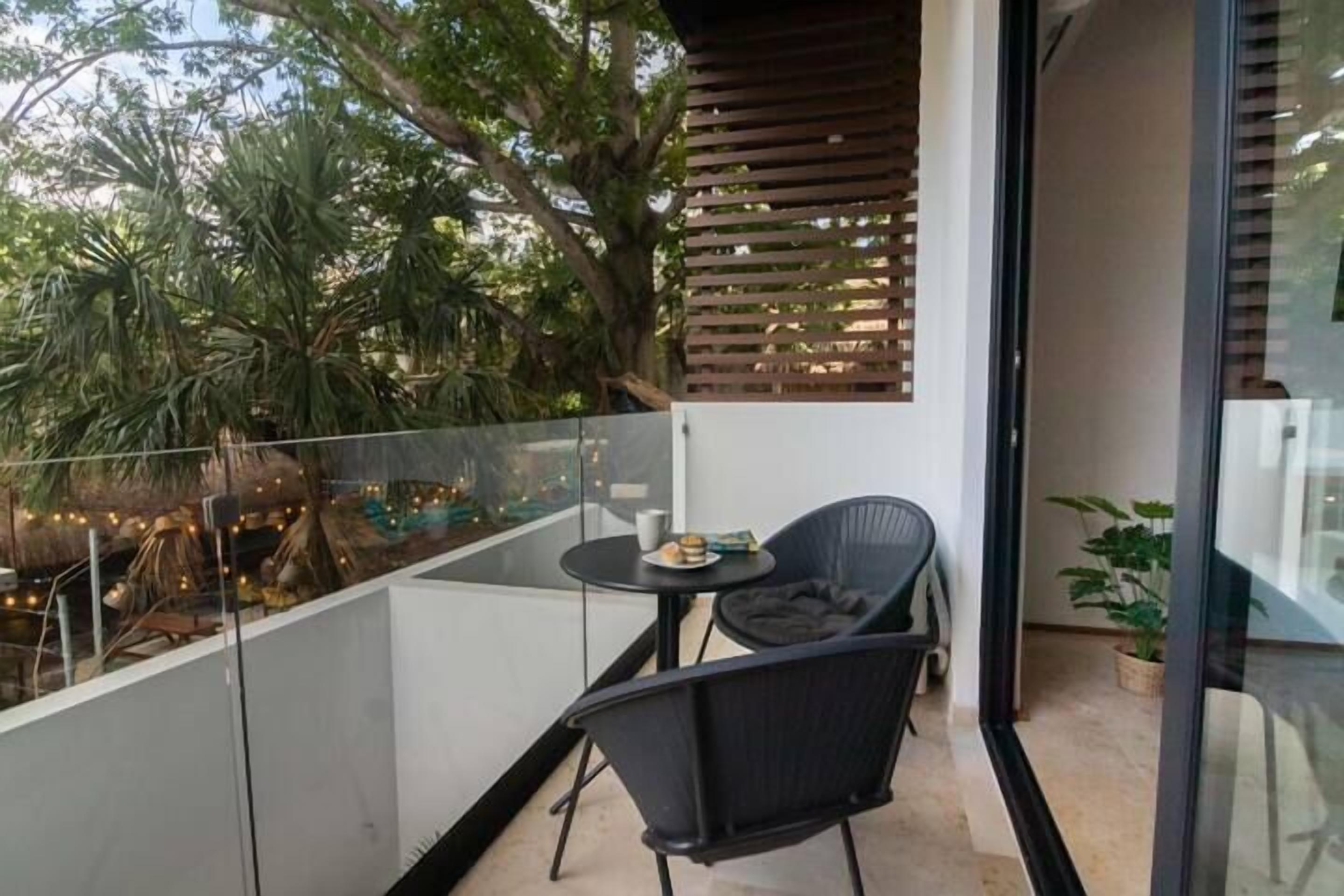 A balcony with a glass railing, a small round table with a chair, and a potted plant.