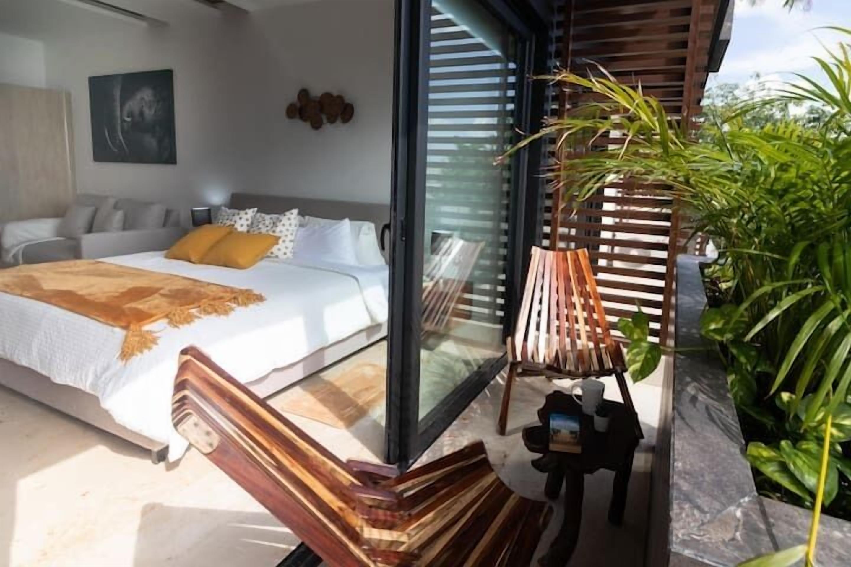 Un dormitorio moderno con una cama grande, un ventanal de vidrio que da a un balcón y una silla de madera.