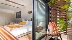 Een moderne slaapkamer met een bed, een glazen deur naar een balkon en een houten stoel.