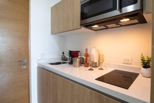 Une cuisine moderne dotée d’un four à micro-ondes encastré, d’un évier en acier inoxydable et d’une plaque de cuisson à induction noire.