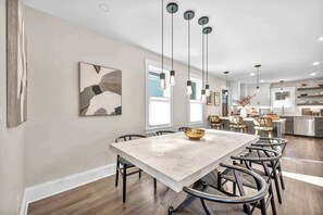A modern dining area with a large table, chairs, pendant lights, and a kitchen in the background. - 2 King Beds | Sauna, Hot Tub & Pickleball Court (Cleveland)