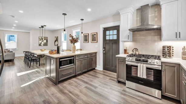 A modern kitchen with stainless steel appliances, wooden flooring, and a dining area with a gray sofa and chairs. - 2 King Beds | Sauna, Hot Tub & Pickleball Court (Cleveland)