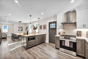 A modern kitchen with stainless steel appliances, wooden flooring, and a dining area with a gray sofa and chairs. - 2 King Beds, Sauna, Hot Tub & Pickleball Court (Cleveland)