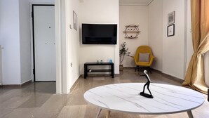 Un salon moderne avec un téléviseur à écran plat, un fauteuil jaune, une table ronde en marbre et une porte donnant sur une autre pièce.
