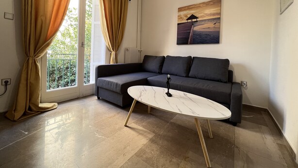 Un salon moderne avec un canapé d’angle gris, une table basse en marbre et un tableau représentant une scène de plage.