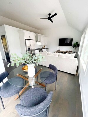 A modern kitchen with white cabinets, a black ceiling fan, and a TV mounted on the wall.