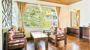 A room with a wooden floor, a table, two chairs, a window with curtains, and a mirror on the wall. - Hotel Blue Poppy (Gangtok)