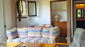 A cozy living room with a wooden ceiling, a sofa set with striped cushions, a wooden armchair, and a small table. - Cocoon de Vacances à L'espinet. Animaux de Compagnie Acceptés (Quillan)