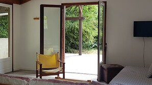 A room with a wooden bed, a chair, and a television. There is a large window and a door leading outside. - Cocoon de Vacances à L'espinet. Animaux de Compagnie Acceptés (Quillan)
