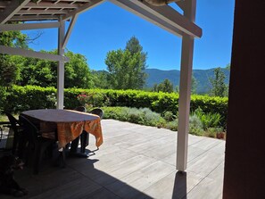 An outdoor patio with a table and chairs, a pergola, and a view of mountains and greenery.