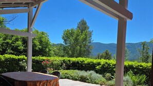 A covered outdoor seating area with a table and chairs, surrounded by lush greenery and a view of mountains. - Cocoon de Vacances à L'espinet. Animaux de Compagnie Acceptés (Quillan)