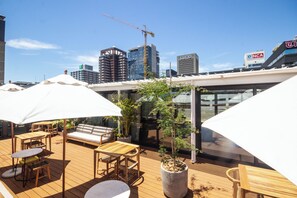 A rooftop terrace with outdoor seating, potted plants, and a view of the city skyline. - Studio With Large Balcony (Cape Town)