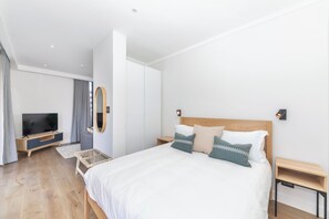 A modern hotel room with a large bed, a TV, a wooden nightstand, and a wall-mounted mirror.