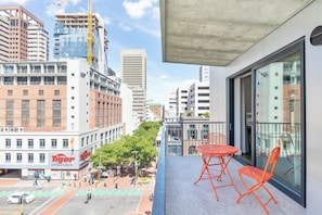 A balcony with orange chairs, a view of a cityscape with buildings, and a street with cars and pedestrians.