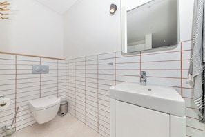 A bathroom with a toilet, sink, mirror, and tiled walls.