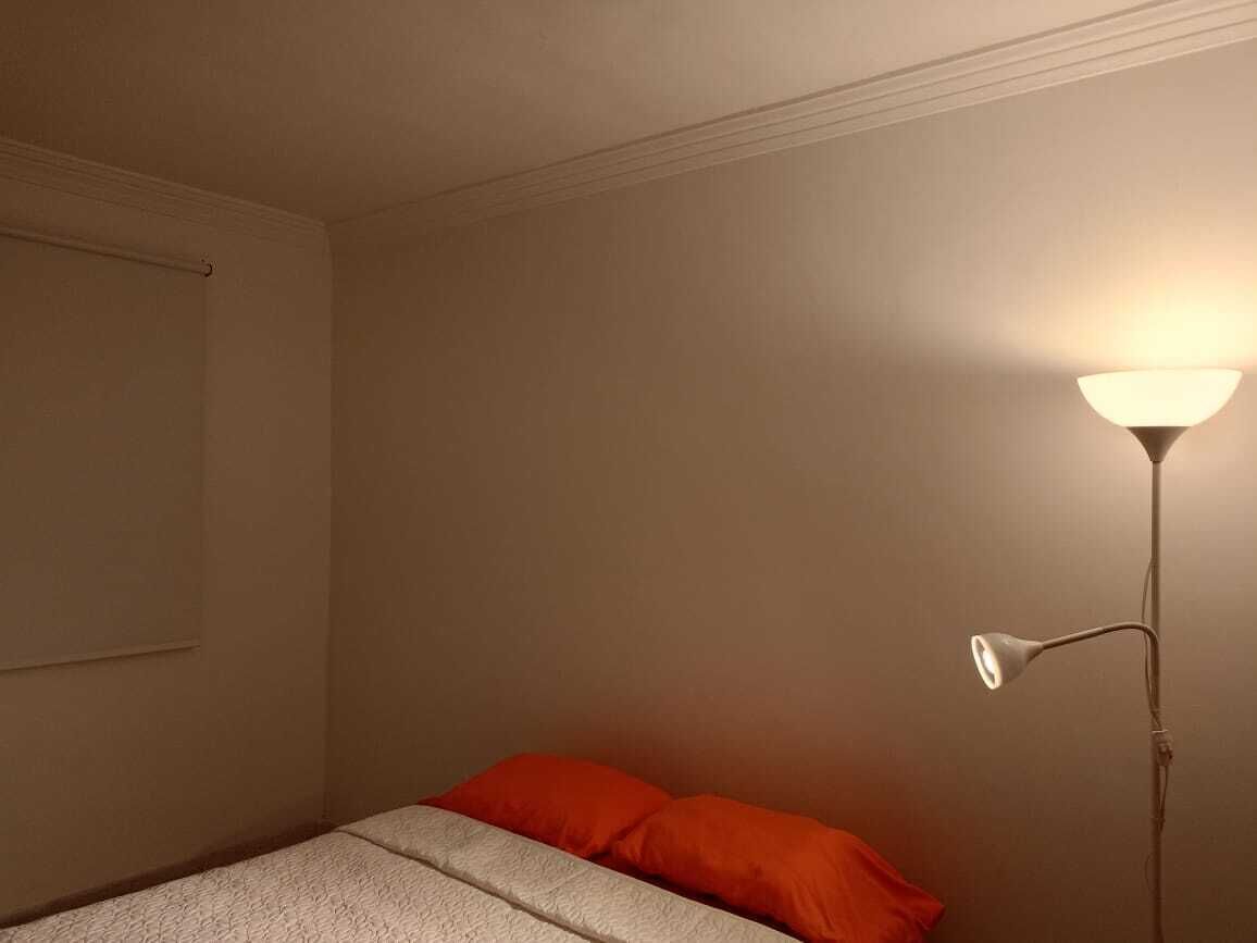 Ein Schlafzimmer mit einem Bett, einem roten Kissen und einer Stehlampe.
