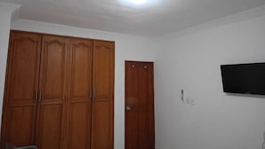 A room with a wooden wardrobe, a door, a wall-mounted TV, and a ceiling light.