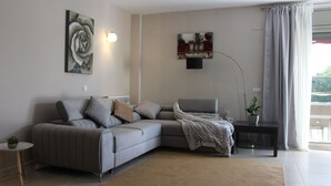 Een moderne zithoek met een grijze modulaire bank, een klein rond tafeltje met een plant en een groot raam met gordijnen.