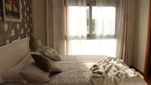 Een slaapkamer met een bed, kussens, een deken en een raam met gordijnen.