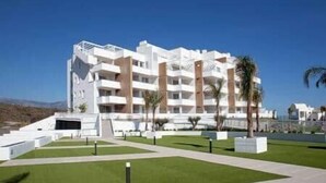 Hotel de vários andares com design moderno, com varandas e um jardim frontal bem cuidado.