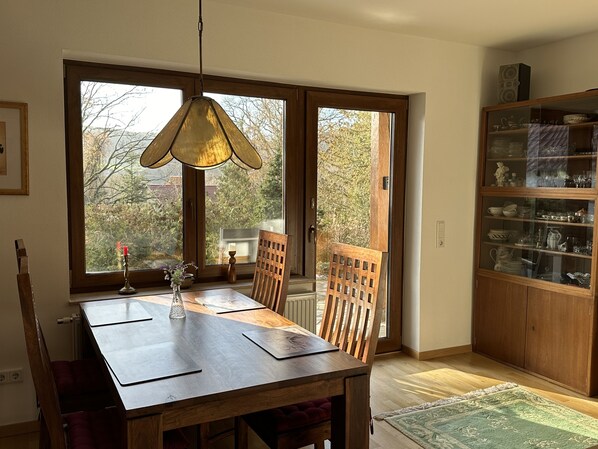A dining area with a wooden table and chairs, a hanging light fixture, and a view through a glass door to the outdoors. - Schöne Ferienwohnung im Landhaus (Dermbach)
