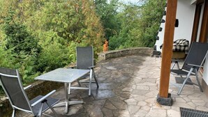Een terras buiten met stenen vloer, twee metalen stoelen, een tafeltje en een houten pilaar.