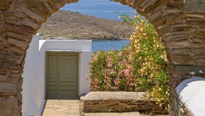 Un arco de piedra que da paso a un edificio blanco con una puerta verde, rodeado de plantas florecientes.